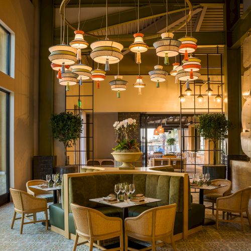 Luxurious dining area with round chandeliers, green booths, wooden chairs, set tables, and potted plants creating an elegant, cozy restaurant vibe.