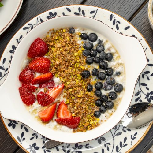 A bowl of creamy yogurt topped with sliced strawberries, blueberries, and crunchy granola on a patterned plate.