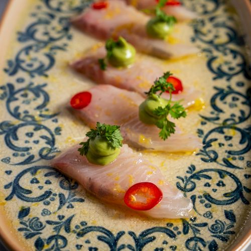 A plate of thinly sliced raw meat (carpaccio) topped with cherry tomatoes, green herbs, and chili oil.