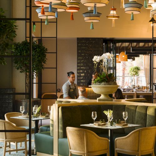 A stylish restaurant interior with hanging globe chandeliers, a large fountain centerpiece, diners seated at tables, and warm lighting.