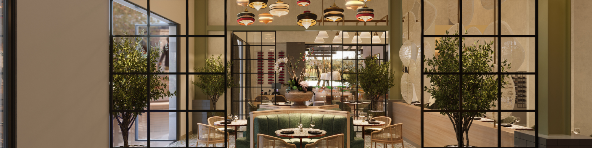 A stylish restaurant interior with a central green banquette, glass-paned walls, warm lighting, potted trees, and multiple tables set for dining.