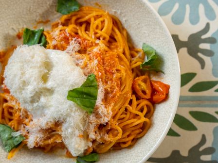 A bowl of spaghetti topped with tomato sauce, grated cheese, and fresh basil on a patterned tablecloth.